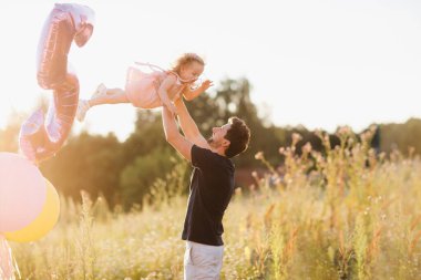 Baba ve kızı gün batımında sokakta yürüyecekler. Babam kızını kollarına atıyor. Mutlu aile anları
