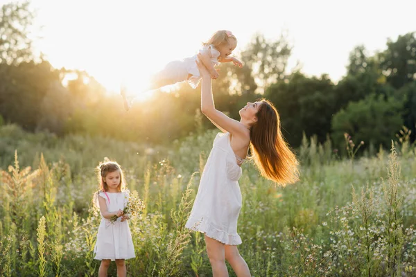 Szczęśliwa rodzina spaceruje w naturze. Mama rzuca ich dzieci. Mama i dwie córki. — Zdjęcie stockowe