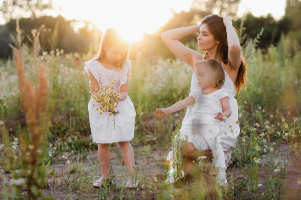 Szczęśliwa rodzina spaceruje w naturze. Mama rzuca ich dzieci. Mama i dwie córki. — Zdjęcie stockowe