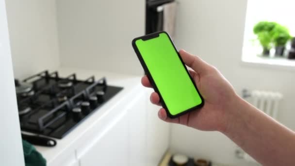 Mockup bild av handen håller svart mobiltelefon med tom grön skärm och bakgrund modern interiör — Stockvideo