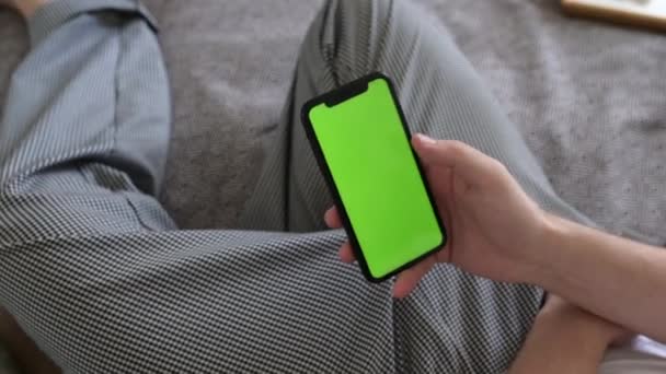 Ο άνθρωπος στο σπίτι ξαπλωμένος σε έναν καναπέ χρησιμοποιώντας Smartphone με πράσινη οθόνη Mock-up, κάνει Swiping. Τύπος που χρησιμοποιεί κινητό τηλέφωνο — Αρχείο Βίντεο