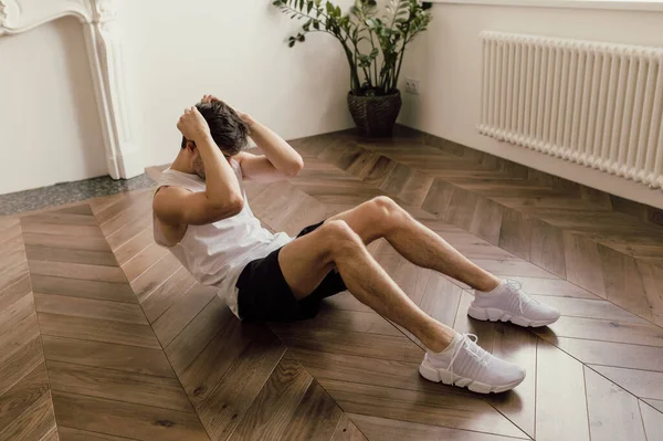 Ο μυώδης νεαρός όμορφος λευκός άντρας γυμνάζεται στο πάτωμα του σπιτιού του κάνοντας μια ρουτίνα ABS και εκπαιδεύοντας τους μυς του. — Φωτογραφία Αρχείου