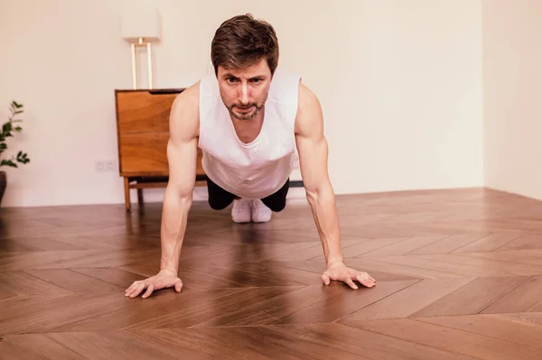 Мускулистый спортсмен делает упражнения на дому в своей яркой квартире с минималистическим интерьером — стоковое фото