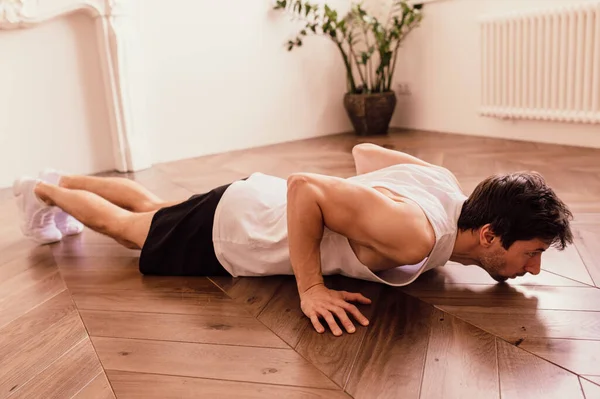 Мускулистый спортсмен делает упражнения на дому в своей яркой квартире с минималистическим интерьером — стоковое фото