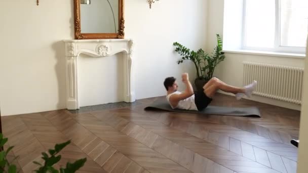 Musculoso joven y guapo hombre blanco está haciendo ejercicio en el suelo de su casa haciendo una rutina de ABS y entrenando sus músculos centrales — Vídeo de stock