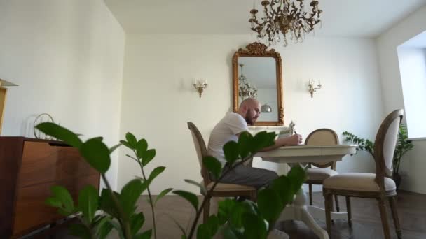 Sebevědomý mladý muž sedí u svého stolu doma, otevírá a začíná používat notebook. V pozadí obývací pokoj s útulným designem — Stock video