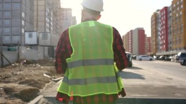 Hard Hat Holds 'un planlarını giyen, Modern İnşaat Alanında Yürüyen Profesyonel İşçi Çekiminin ardından