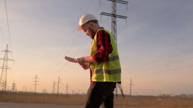 İnşaat alanında yürüyen genç mühendisler, arka planda büyük vinç, güvenlik ekipmanları giyiyorlar.