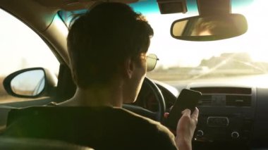 Makineyi kullanırken akıllı telefon kullanan sıradan bir genç adam. Bir adam araba sürerken cep telefonundan navigatör haritasına bakar..