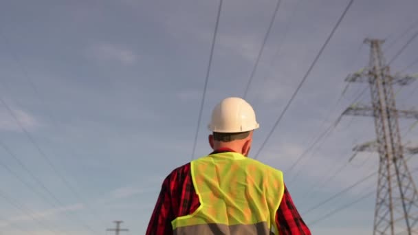 Siguiendo Shot of Professional Worker Usando casco duro sostiene plano, Caminando a través de líneas eléctricas — Vídeos de Stock