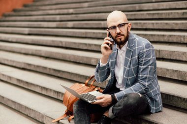  Dizüstü bilgisayarı ve akıllı telefonu olan bir yönetici. Dışarıda dizüstü bilgisayarda çalışan adam.