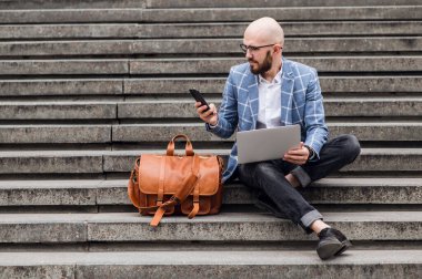  Dizüstü bilgisayarı ve akıllı telefonu olan bir yönetici. Dışarıda dizüstü bilgisayarda çalışan adam.