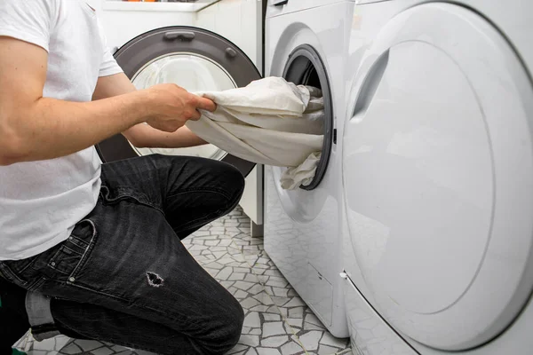 Молодой человек пользуется стиральной машиной дома. День прачечной — стоковое фото