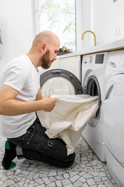 Молодой человек пользуется стиральной машиной дома. День прачечной — стоковое фото