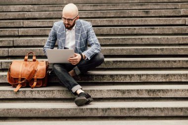  Deri çantalı genç adam merdivenlerde oturuyor.