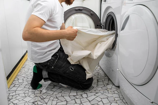 Человек кладет белье в стиральную машину — стоковое фото