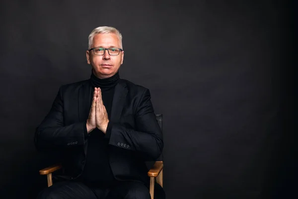emotional middle aged man in a black suit clasps his hands in a prayer gesture