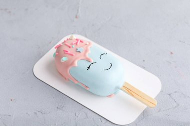 Gri arka planda beyaz bir tabakta gülümseyen buzlu pasta.