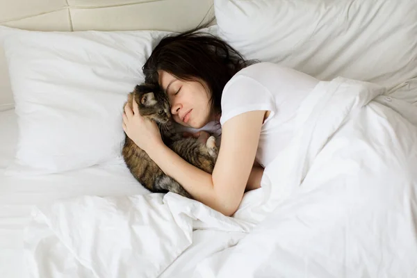 Bela menina sorridente com os olhos fechados deitado na cama e abraçando gato — Fotografia de Stock