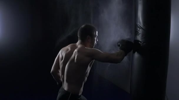 Fotografía cinematográfica en cámara lenta del boxeador masculino golpeando un saco de boxeo en un estudio de boxeo. Hombre boxeador entrenamiento duro — Vídeo de stock