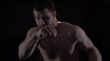 Hafif spor salonunda kickboxçu eğitimi. Sporcu kamerada boks yapıyor. Muay thai dövüşçüsü yumruk atıyor. Koyu arkaplanda siluet