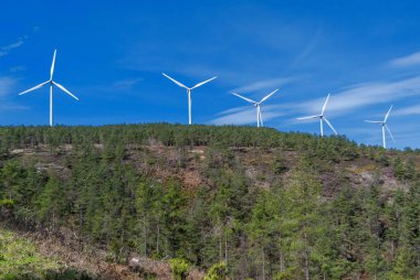 Beyaz rüzgar elektrik türbinleri, orman, dağlar ve baharda mavi gökyüzü.