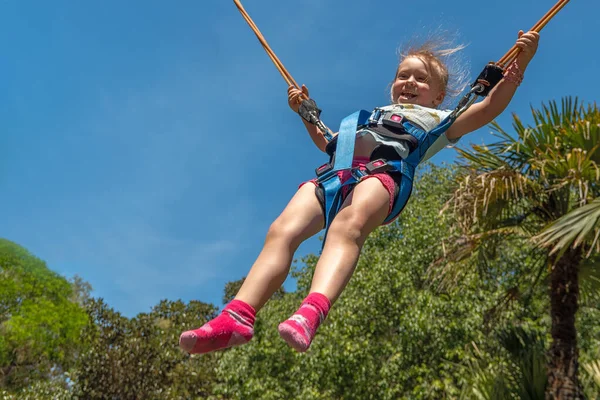 Parktaki bungee trambolinde zıplayan mutlu kız. Palmiye ağaçlarının ve mavi gökyüzünün arka planı.