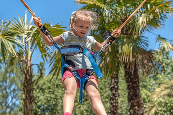 Parktaki bungee trambolinde zıplayan mutlu kız. Palmiye ağaçlarının ve mavi gökyüzünün arka planı.