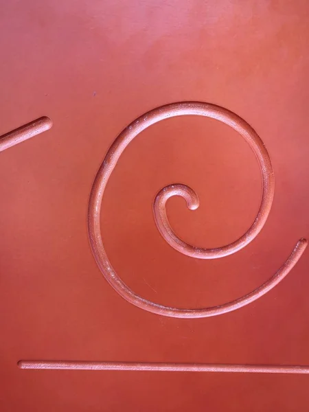 Spiral and straight line carved on a wooden plane covered with red paint