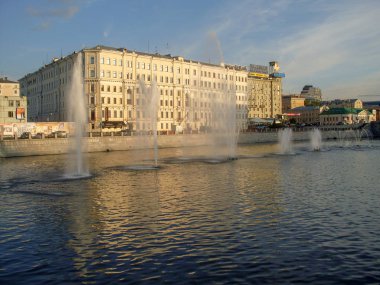 Fountains on the water and a multi storey building in the background in the sun