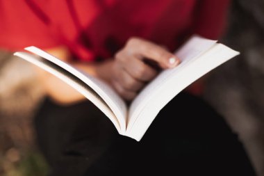 Ortadaki açık bir kitabın kapağını kapat. Genç bir kadın, sayfanın tek kelimesini işaret ediyor. Alçak alan derinliği.