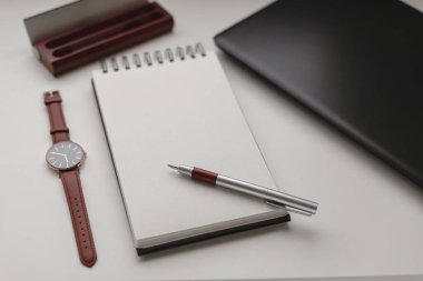 Boş bir sayfası ve iş yeri arka planı olan açık spiral bir defterin yüksek görüş açısı. Laptop, kalem, kalem kutusu ve bir saat. Çalışma, iş, serbest çalışma kavramı.