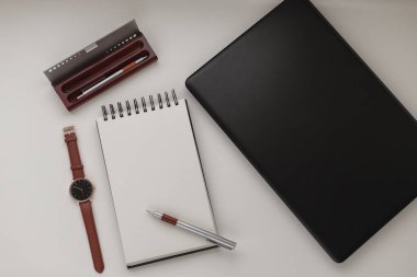 Dizüstü bilgisayarı, kalemi, kalem kutusu, kol saati ve defteri olan minimalist çalışma alanı. Beyaz ofis masası çerçevesi. Çalışmak, iş yapmak, serbest çalışmak. Boşluğu kopyala, üst görünüm, düz yatış, model.