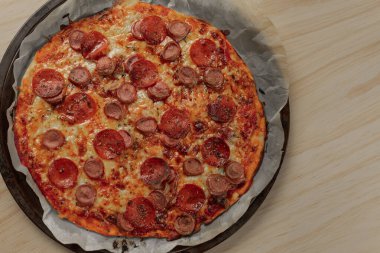 Ev yapımı pepperoni ve metal tepside siyah bir peçeteyle ahşap bir masada sosisli pizza.