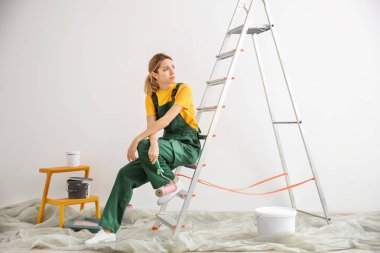 Genç kadın dekoratör boş odada boya silindiri ile üzgün