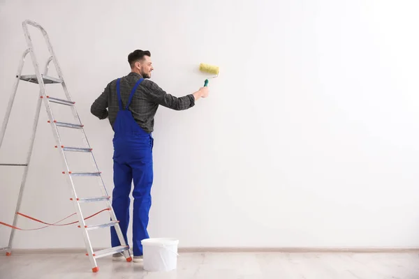 Молодий чоловічий декоратор малює стіну в порожній кімнаті — стокове фото