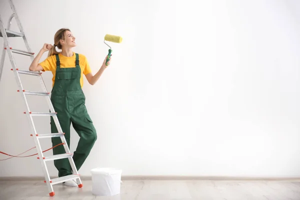 Jonge vrouwelijke decorateur met verfroller in lege ruimte — Stockfoto