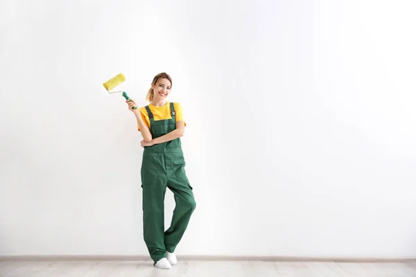 Young female decorator with paint roller in empty room — Stock Photo, Image