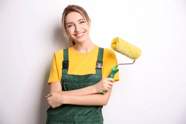 Young female decorator with paint roller on white background — Stock Photo, Image