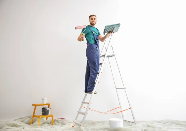 Joven decorador masculino con rodillo de pintura en habitación vacía — Foto de Stock
