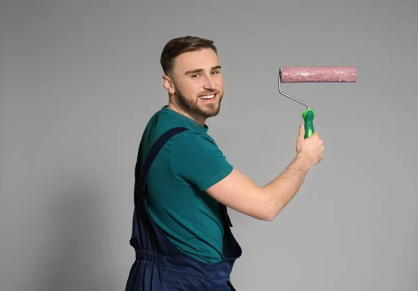 Young male decorator with paint roller on color background — Stock Photo, Image