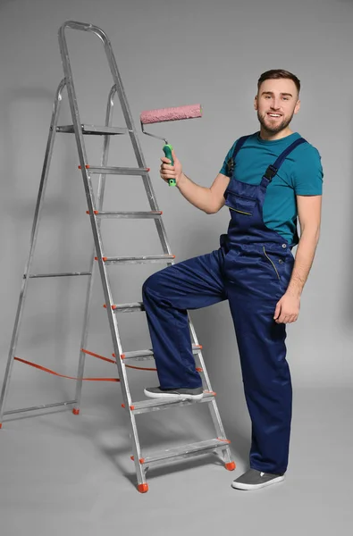 Joven decorador masculino con rodillo de pintura sobre fondo de color —  Fotos de Stock