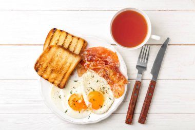 Tabak kızarmış yumurta, pastırma ve Beyaz ahşap zemin üzerinde tost ile