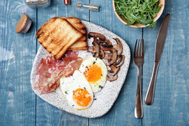 Kızarmış yumurta, pastırma, mantar ve tost ahşap arka plan üzerinde plaka