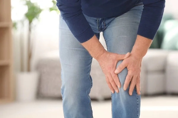 Mature man suffering from knee pain at home — Stock Photo, Image