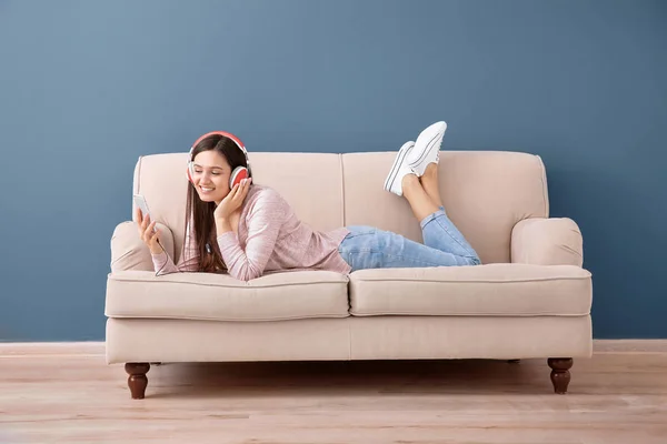Gyönyörű fiatal nő zenét hallgat a kanapén, beltérben — Stock Fotó