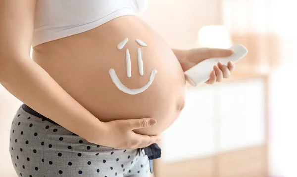 Smile painted with cream on pregnant woman\'s belly against blurred background, closeup