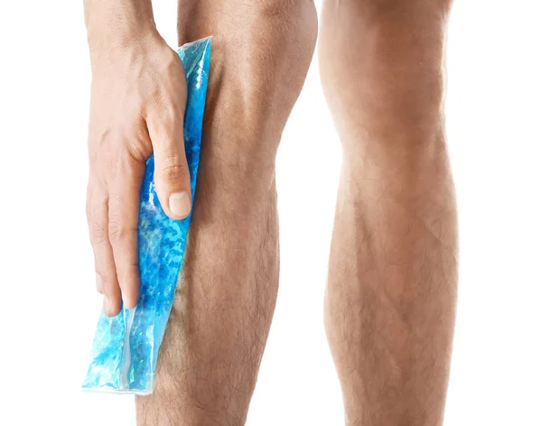 Young man applying cold compress to leg on white background — Stock Photo, Image