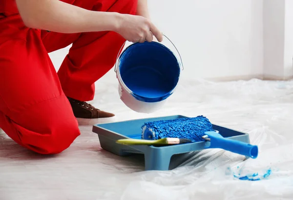 Male decorator pouring paint into tray indoors