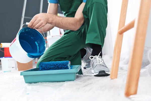 Male decorator pouring paint into tray, closeup